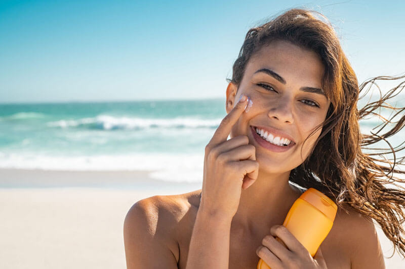 Picture of a smiling woman, happy with her nose surgery she had at Top Plastic Surgeons. The woman has long brown hair and is standing on a sandy Costa Rican beach with the ocean in the background.