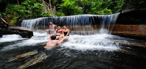 Picture of visitors to a natural waterfall in a Costa Rica Hot Springs spa.  The picture is of four tourists sitting in a pool formed by the hot springs waterfall.