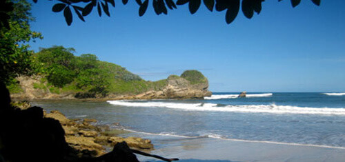 Picture of a beautiful pristine Costa Rica Beach with blue water and gently breaking waves..  The water is blue and the waves white, against a blue sky backdrop.