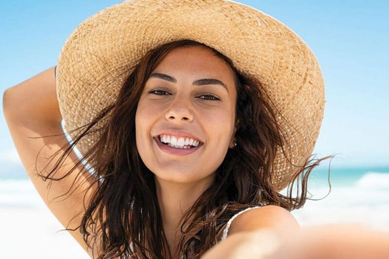 Picture of a on the beach, happy with her plastic surgery at Top Plastic Surgeons in Canada.  The woman is wearing tan sun hat and sitting on a Costa Rica beach.