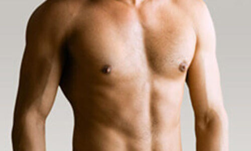 Close-up picture of a man,  happy with his male breast reduction  procedure he had in San Jose, Costa Rica.  The man is shown leaning against the edge of a pool and looking directly at the camera with an arm raised to his head to feature his male breast reduction.