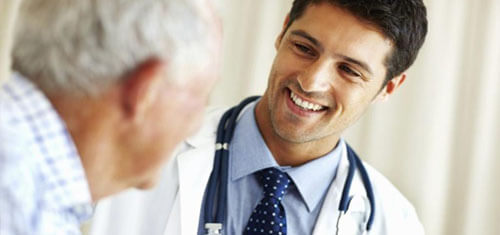 Picture of a doctor representing the top plastic surgeons in Costa Rica.  The picture shows a doctor in a white coat looking at a male patient, and smiling.