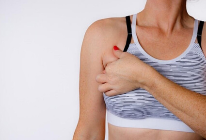 Picture of a woman facing the camera and happy with the perfect bra line liposuction procedure she had at Top Plastic Surgeons in beautiful San Jose, Costa Rica.  The woman is wearing a soft light purple pastel top and holding one hand to the area of her bra line liposuction.