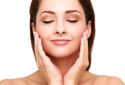 Picture of a woman with long dark brown hair, facing the camera with eyes closed, holding her hands to the side of the cheeks and happy with her perfect face lift with neck lift procedure she had at Top Plastic Surgeons in beautiful San Jose, Costa Rica.