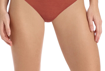 Picture of a trim woman wearing a red bikini bottom, and happy with her perfect thigh lift she had at Top Plastic Surgeons in beautiful San Jose, Costa Rica.  The woman is facing the camera with both arms down to her sides.