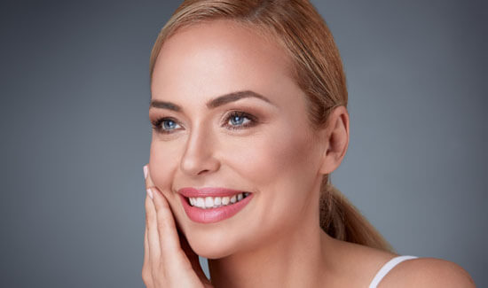 Picture of a smiling woman, facing slightly to the side of the camera and happy with her perfect face lift procedure she had at Top Plastic Surgeons in beautiful San Jose, Costa Rica.  The woman has her hand to the side of her face indicating her happiness with the face lift.